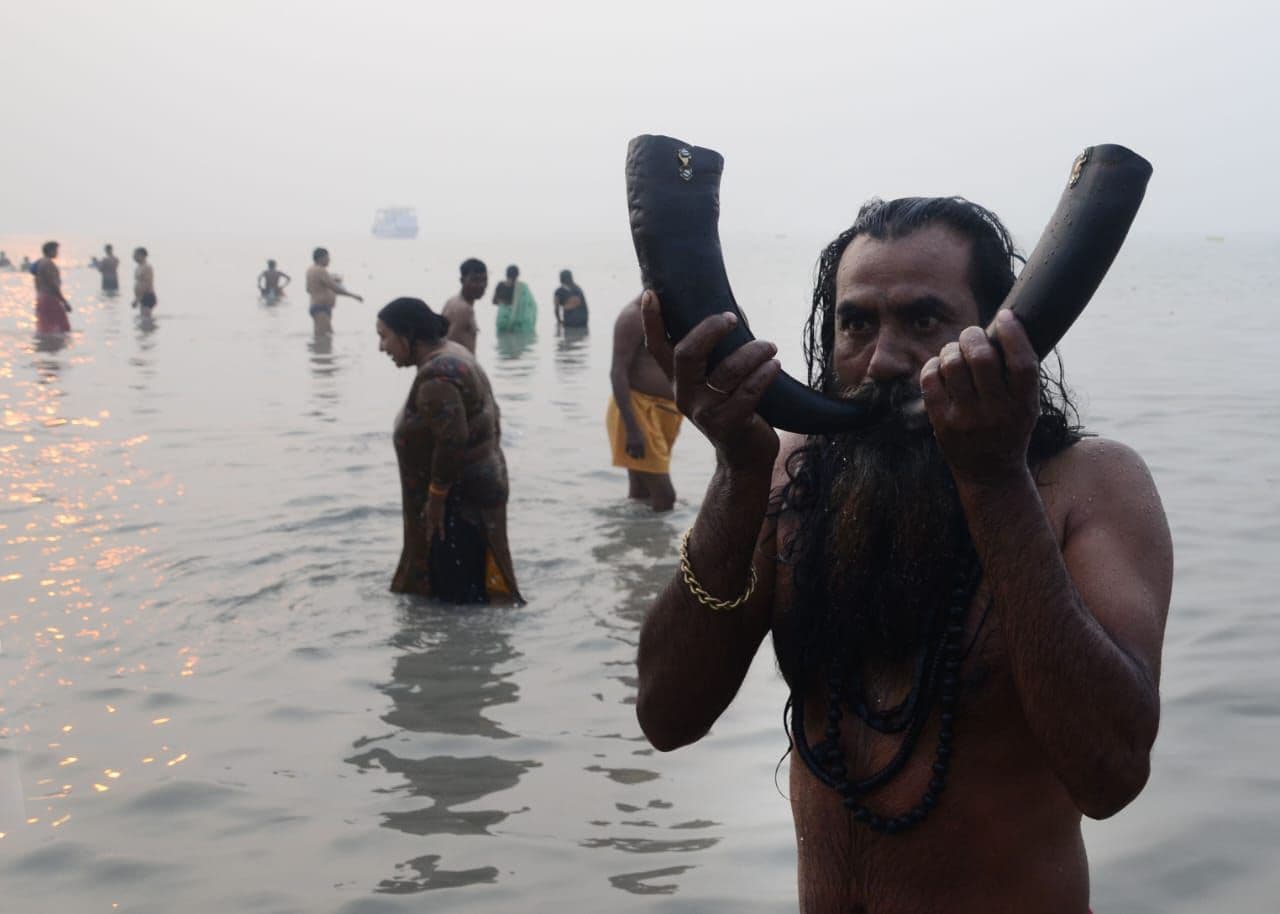 गंगा सागर में स्नान के दौरान वाद्य यंत्र बजाता साधु।